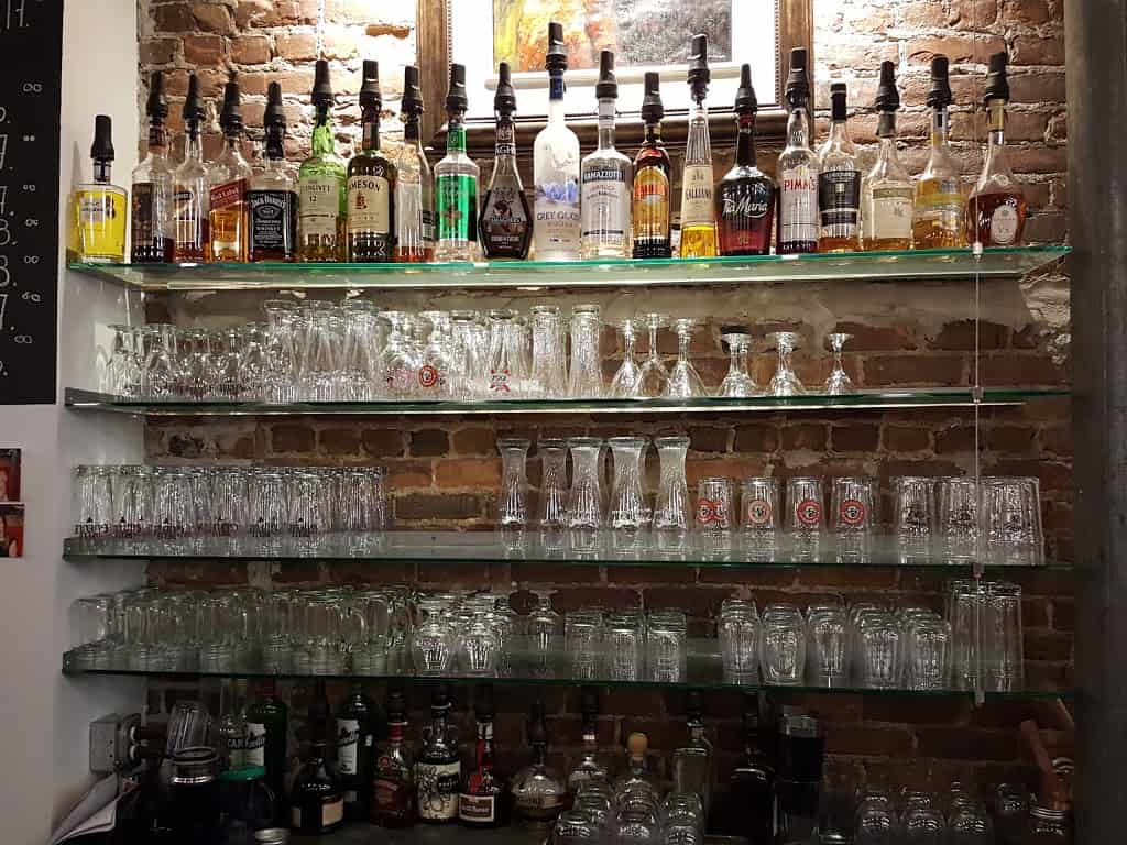 Poutineville Saint-Roch - Étagère en vitre derrière le bar avec bouteilles d'alcools et verre à bière