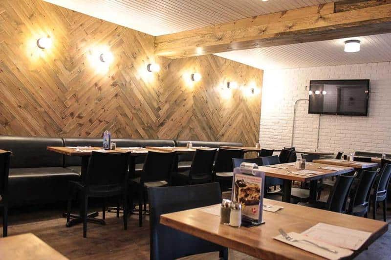 Intérieur du restaurant avec une longue banquette et plusieurs tables. Il a un mur de brique blanche et un mur en bois et une télévision au mur