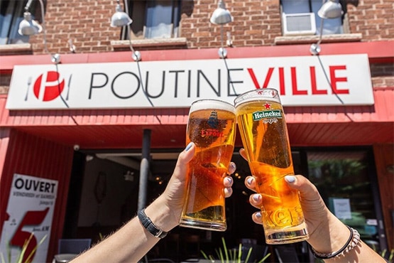 Two friends cheersing with beers in front of Poutineville restaurant