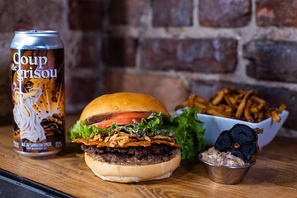 Burger de la BurgerWeek 2022, avec une canette de bière Coup de Grisou, un contenant de frite et une sauce à l'ail noir avec un ail noir coupé en deux.